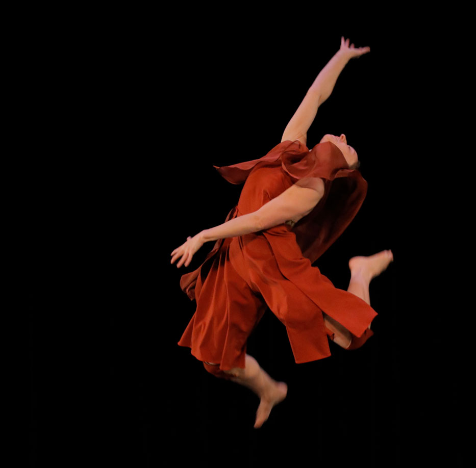 Dance artist jumping in the air with an arm extended and one leg bent back