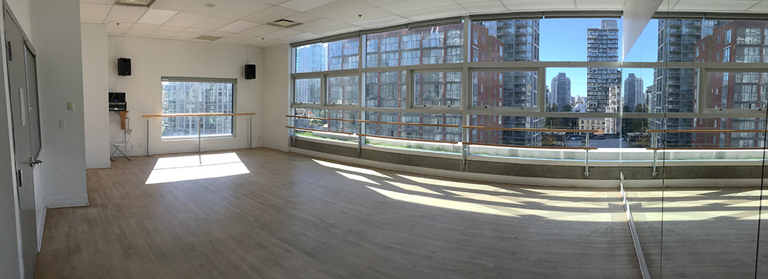 An empty dance studio with bars against the windows with sun streaming through the windows