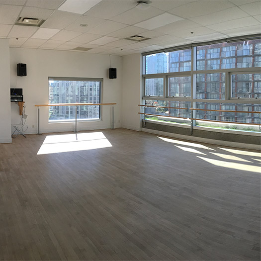 An empty dance studio with bars against the windows with sun streaming through the windows