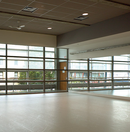 An empty dance studio with mirrors and windows with the blinds half closed.