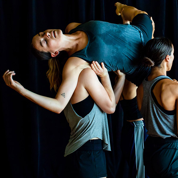 Three dance artists hold another on top of them while posing