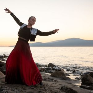 Dance artist Maria Avila poses on a beach while wearing a flamenco costume