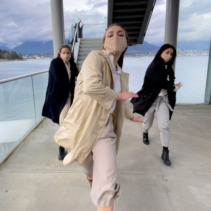 Three dancers walk toward the camera while dancing and wearing masks