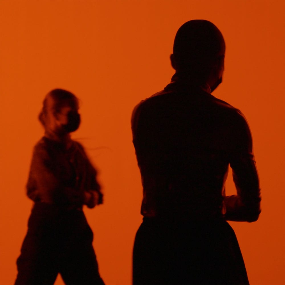 Silhouette of two dance artists in front of an orange background