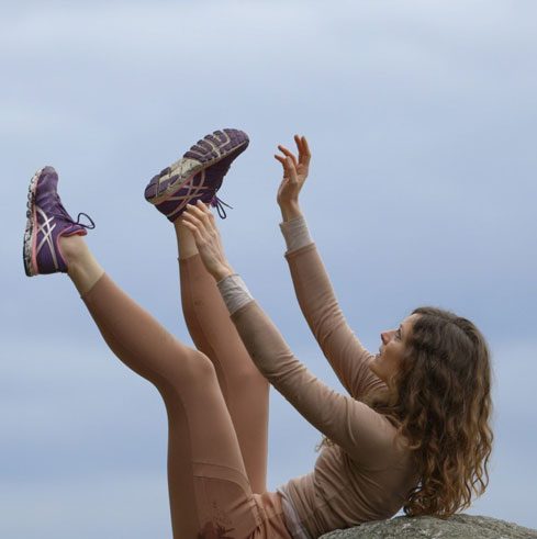 Dance artist Anouk Froidevaux leans on a rock with her legs and arms extended into the air