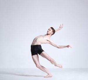 Male dance artist leans backwards with arms and one leg extended