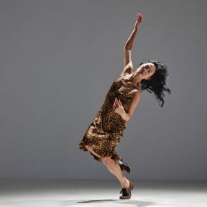 Dance artist Ziyan Kwan poses with one arm above her head, standing on the ball of one foot
