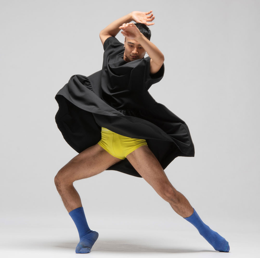 Dance artist Justin Calvadores posing mid twirl with his arms above his head and his dress swirling around him