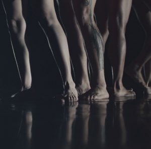 Multiple sets of bare legs and feet standing on a reflective floor