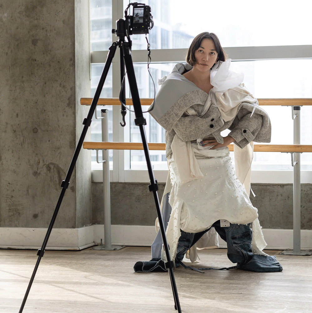 A dance artist looks at an in frame camera. They are wearing various clothing items that have been deconstructed.
