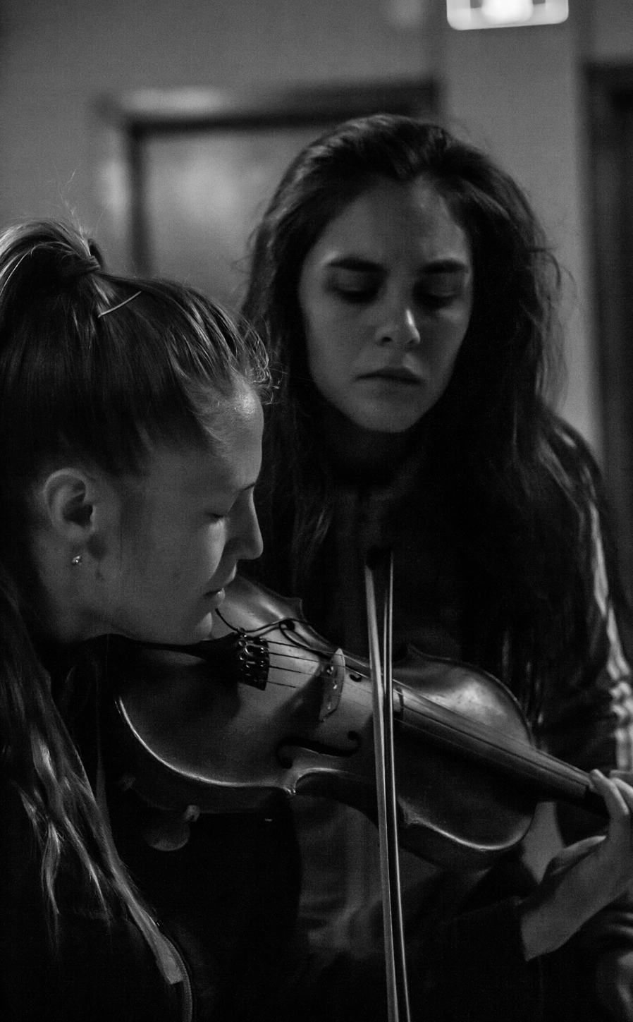Dance artist Rebecca Margolick watches musician Hannah Epperson while she plays she plays the violin. Both have their eyes closed. This image is in greyscale.