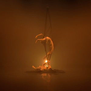 Two dancers on a hazy orange stage. One is hanging from ropes and the other is lying on the stage, holding the ropes.