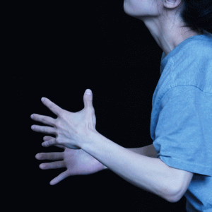 A close up of hands extended outwards of a dance artist - she is wearing a blue t shirt and you can just see a bit of her chin which is tipped up.